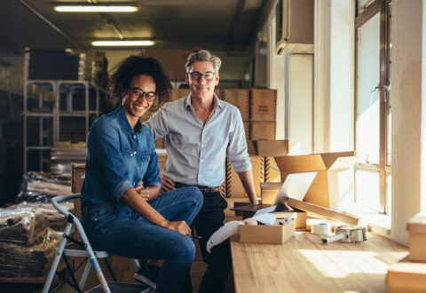 Successful online shop business partners in a small office. Male and female entrepreneurs at their online shop warehouse looking at camera and smiling.